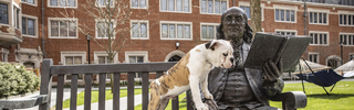 Handsome Dan sitting next to Ben Franklin statue with paws on Franklin's thigh